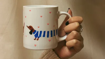 Hand hält Tasse mit Dackel-Motiv.