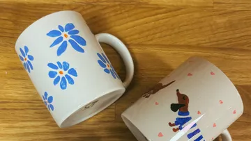 Zwei Tassen mit Blumen- und Hundemotiven auf Holz.