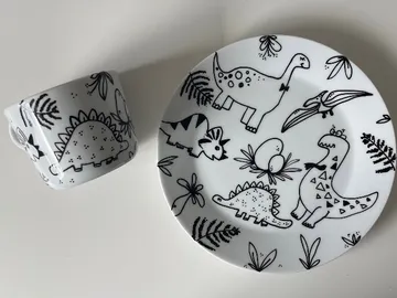 A plate and mug with dinosaur patterns on a white background.
