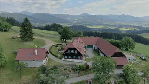 Bauernhaus auf Hügel mit Bergkulisse.