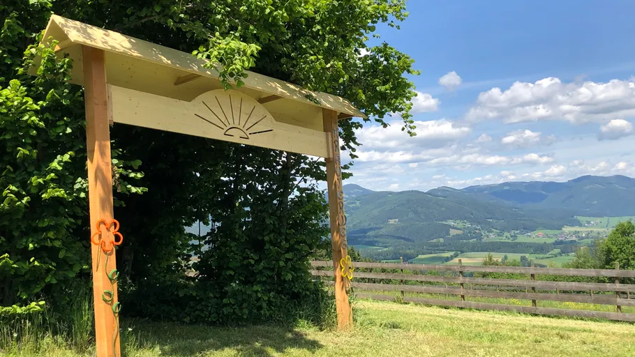 Holzbogen mit Sonnendesign in Bergnähe.