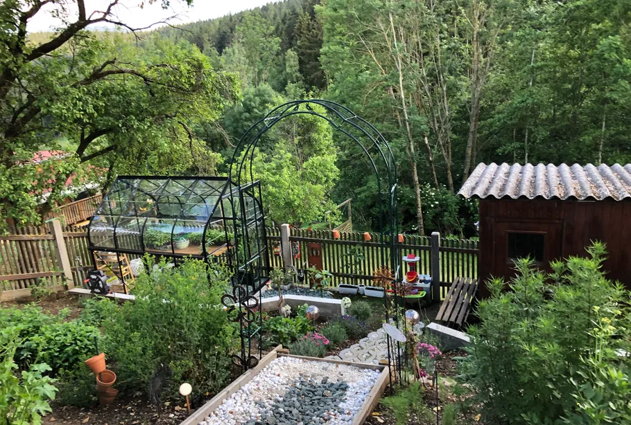 Garten mit Gewächshaus, Bogen und Schuppen.