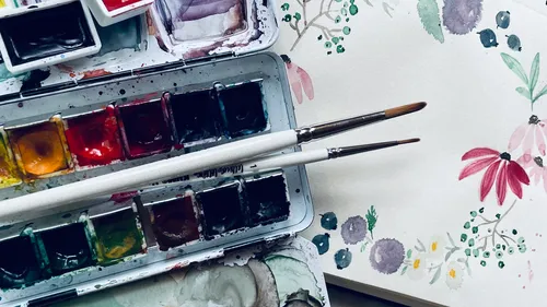 Aquarelle und Pinsel mit Blumenmalerei.