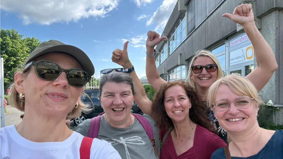 Five smiling women outdoors near a building.