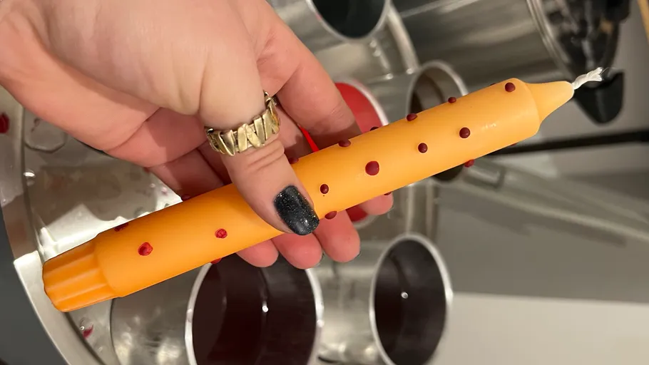 Hand holding a yellow candle with red dots.