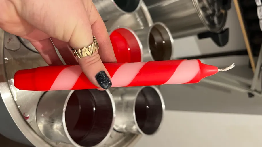 Hand hält rot gestreifte Kerze im Workshop.