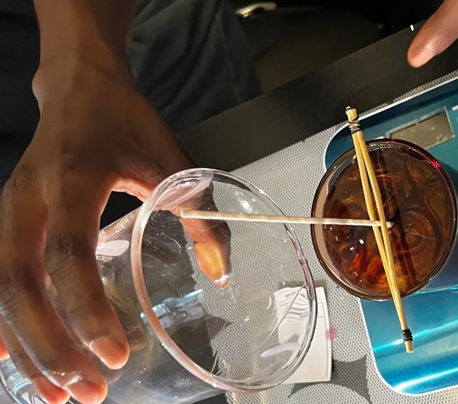 Hand balancing chopstick on cup with drink.