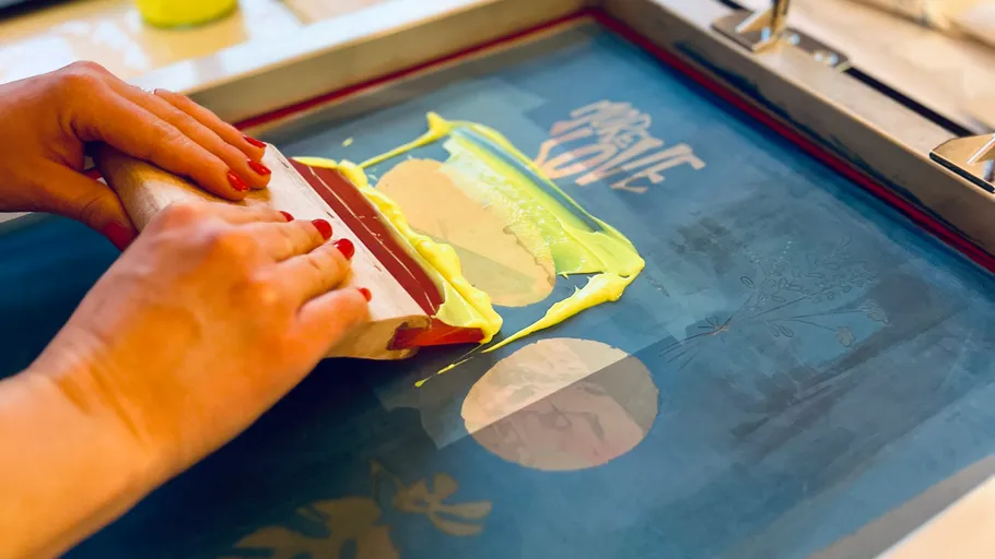 Hände beim Siebdruck mit gelber Tinte.