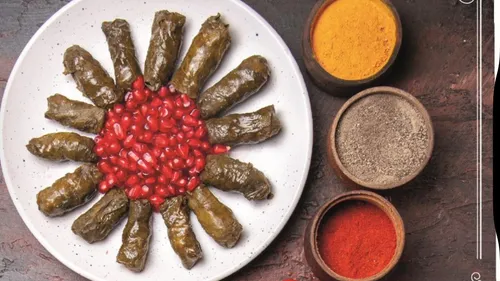 Stuffed grape leaves with pomegranate seeds, spices nearby.