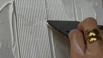 Hand spreading white paste with toothed tool.