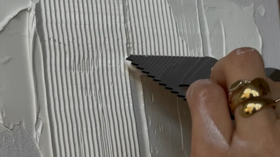 Hand verteilt weiße Paste mit gezahntem Werkzeug.