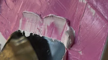 Palette knife spreads pink paint on surface.