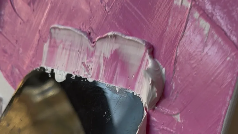 Palette knife spreads pink paint on surface.