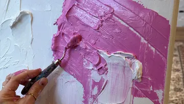 Hand trägt rosa Farbe auf Leinwand auf.