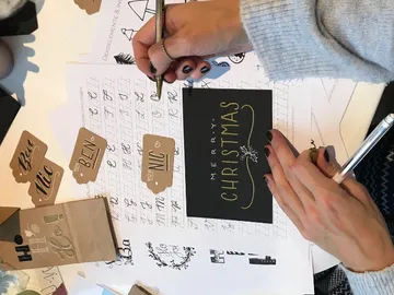 Eine Hand schreibt auf eine Weihnachtskarte in einem kreativen Umfeld.