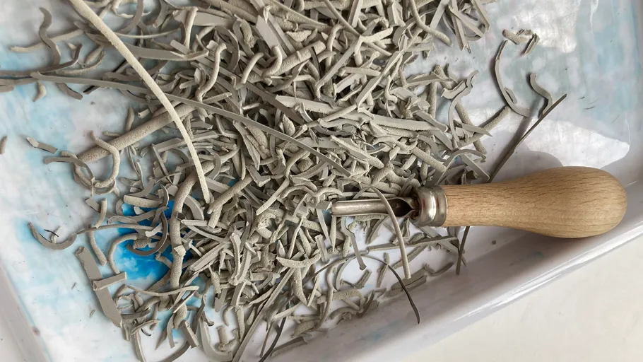 Clay shavings with carving tool in tray.