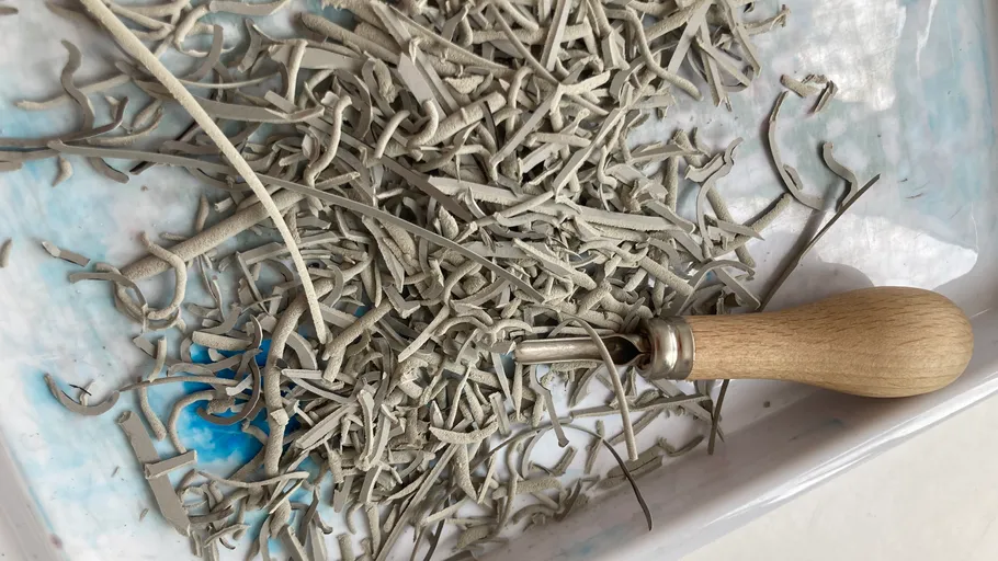 Clay shavings and tool on white tray.