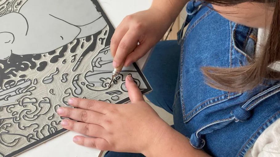 Person carving intricate design on linoleum.