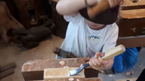 Child carving wood in a workshop.
