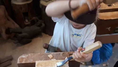 Kind schnitzt Holz in einer Werkstatt.