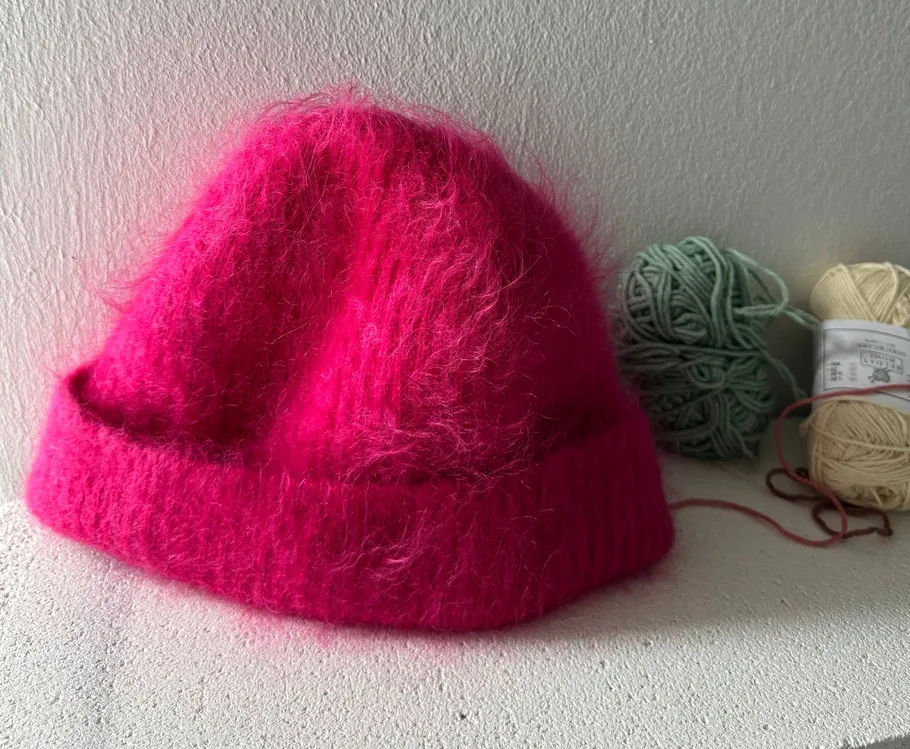 Pink knitted hat beside yarn balls.
