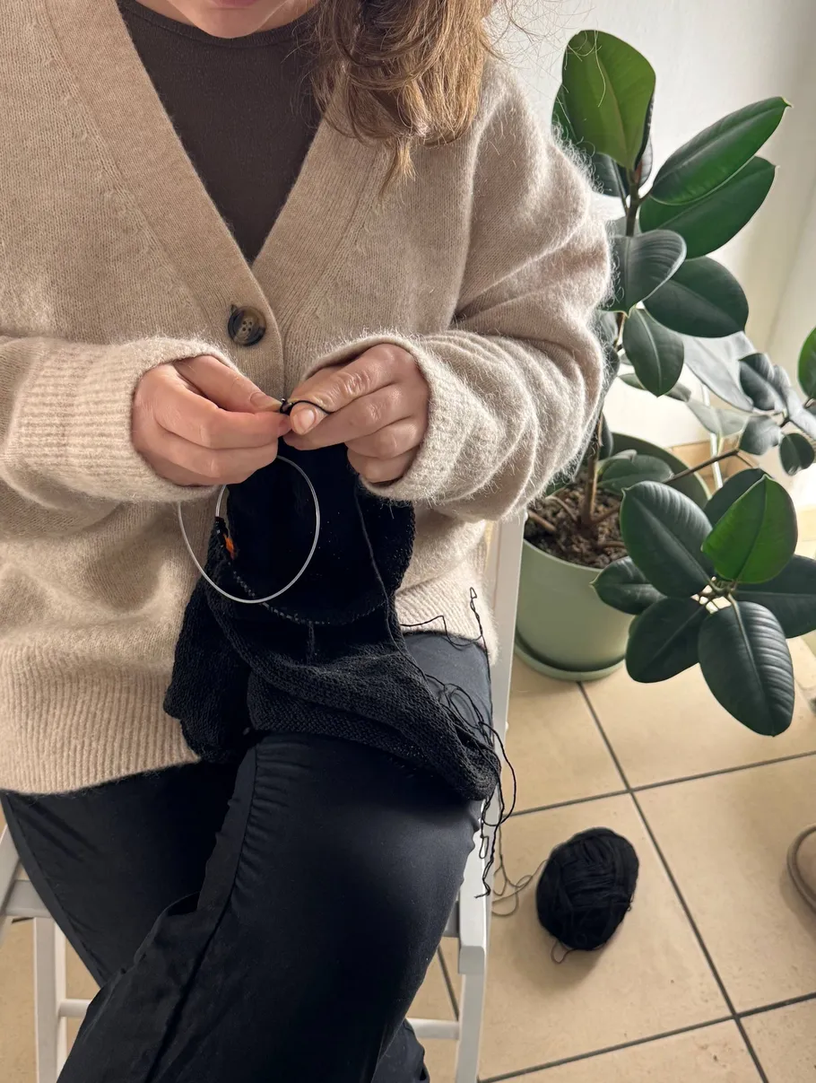 Person knitting with a plant nearby indoors.