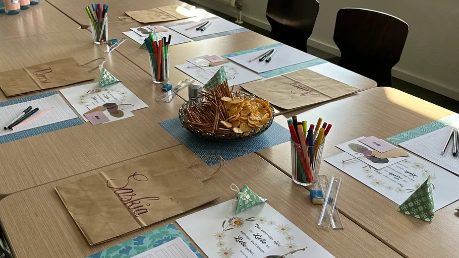 Klassenzimmertisch mit Tüten und Materialien gedeckt.