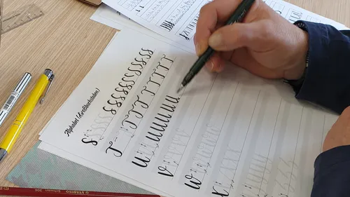 Person practicing calligraphy on lined paper.