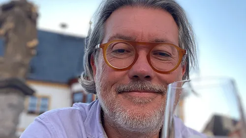 Man with glasses holding a glass outdoors.