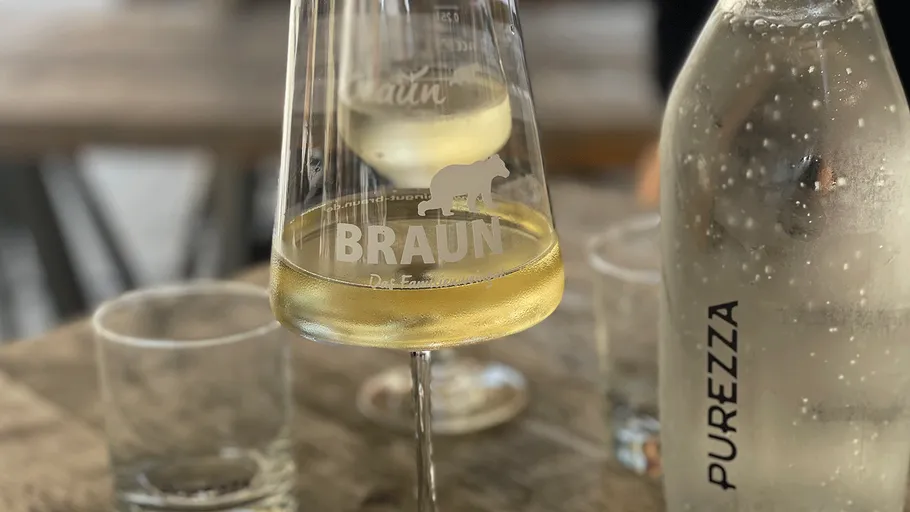 Weinglas, Weißwein, neben Wasserflasche.