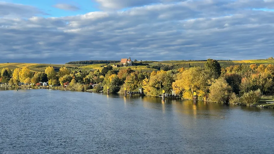 Fluss fließt neben herbstfarbenen Bäumen und Hügeln.