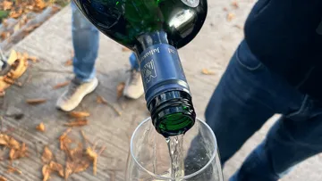 Wine bottle pouring into glass outdoors.