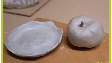 Clay apple and plate on cardboard surface.
