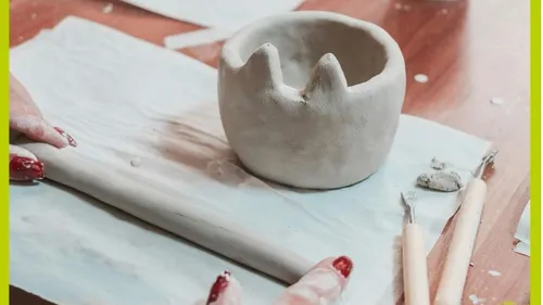 Hands shaping clay near unfinished pottery cup.