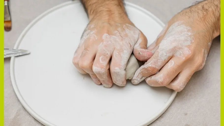 Hands kneading clay on a white surface.
