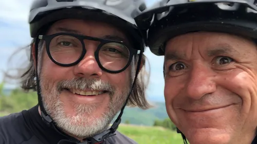 Two cyclists smiling, wearing helmets outdoors.