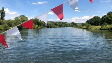 Red and white flags over a river scene.