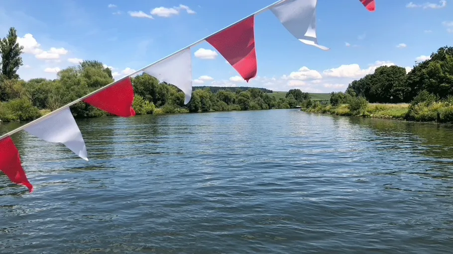 Red and white flags over a river scene.