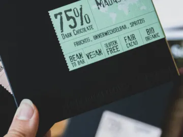 The chocolate bar is held; it shows nutritional information.