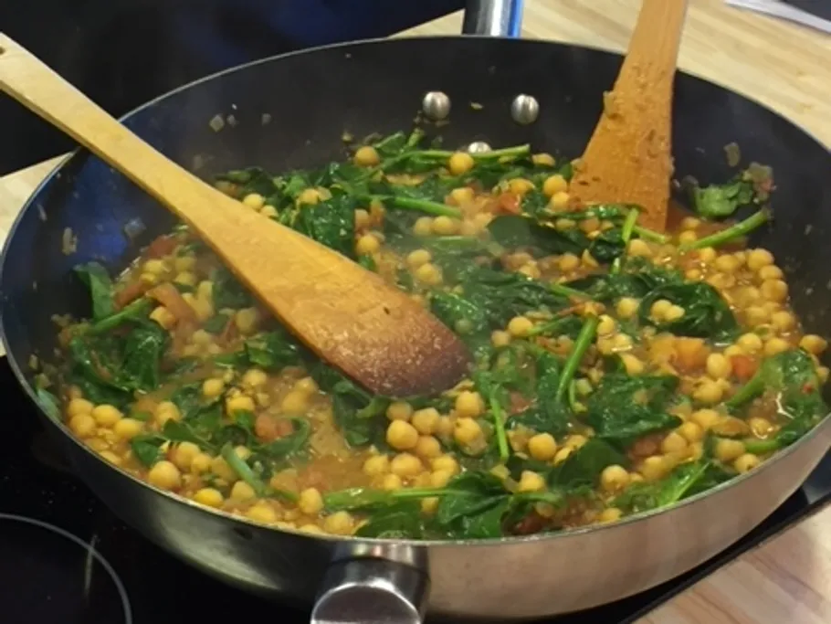 Cookware with spinach and chickpeas is stirred.