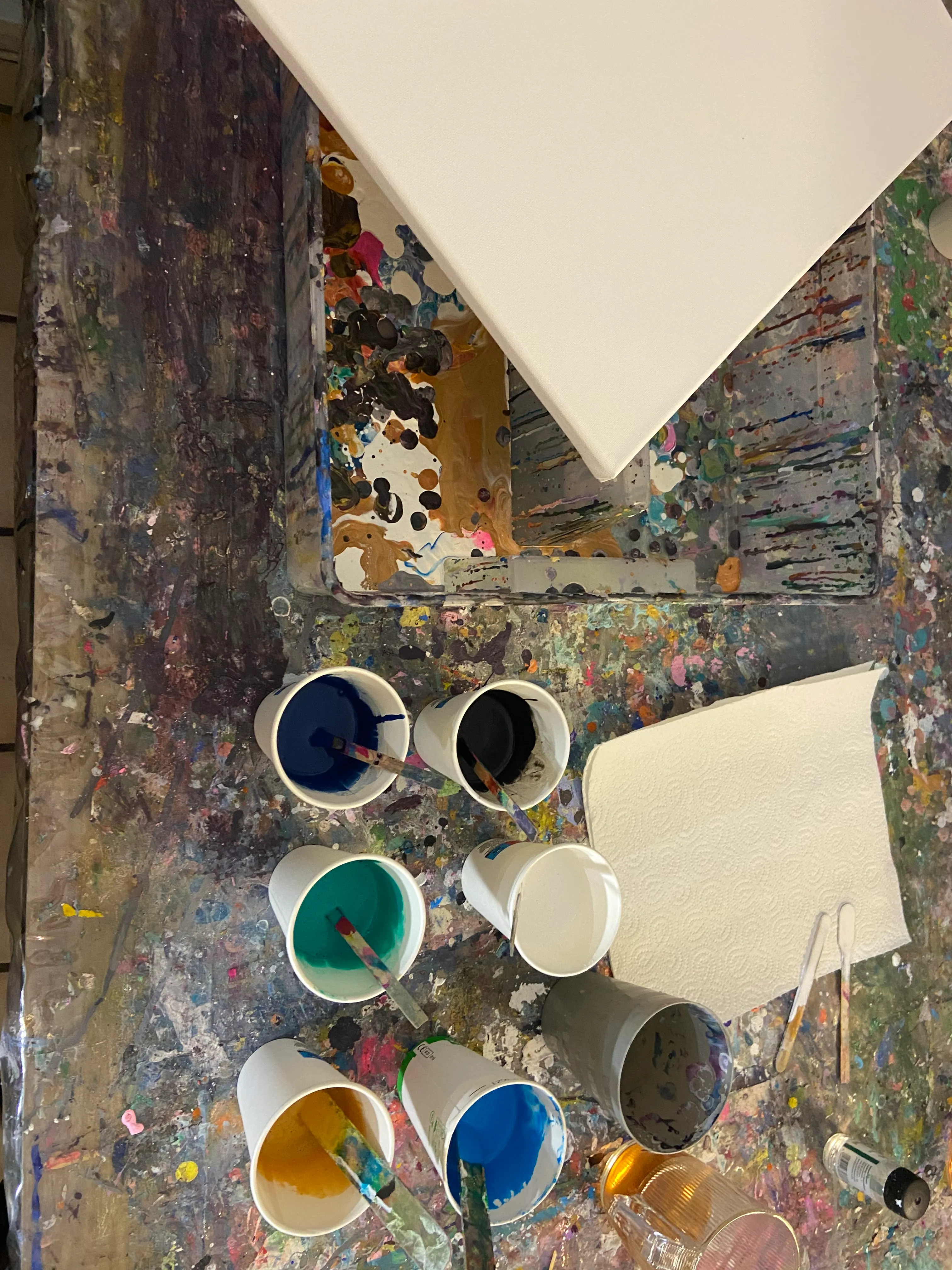 Farbbecher mit Pinseln auf unordentlichem Tisch.