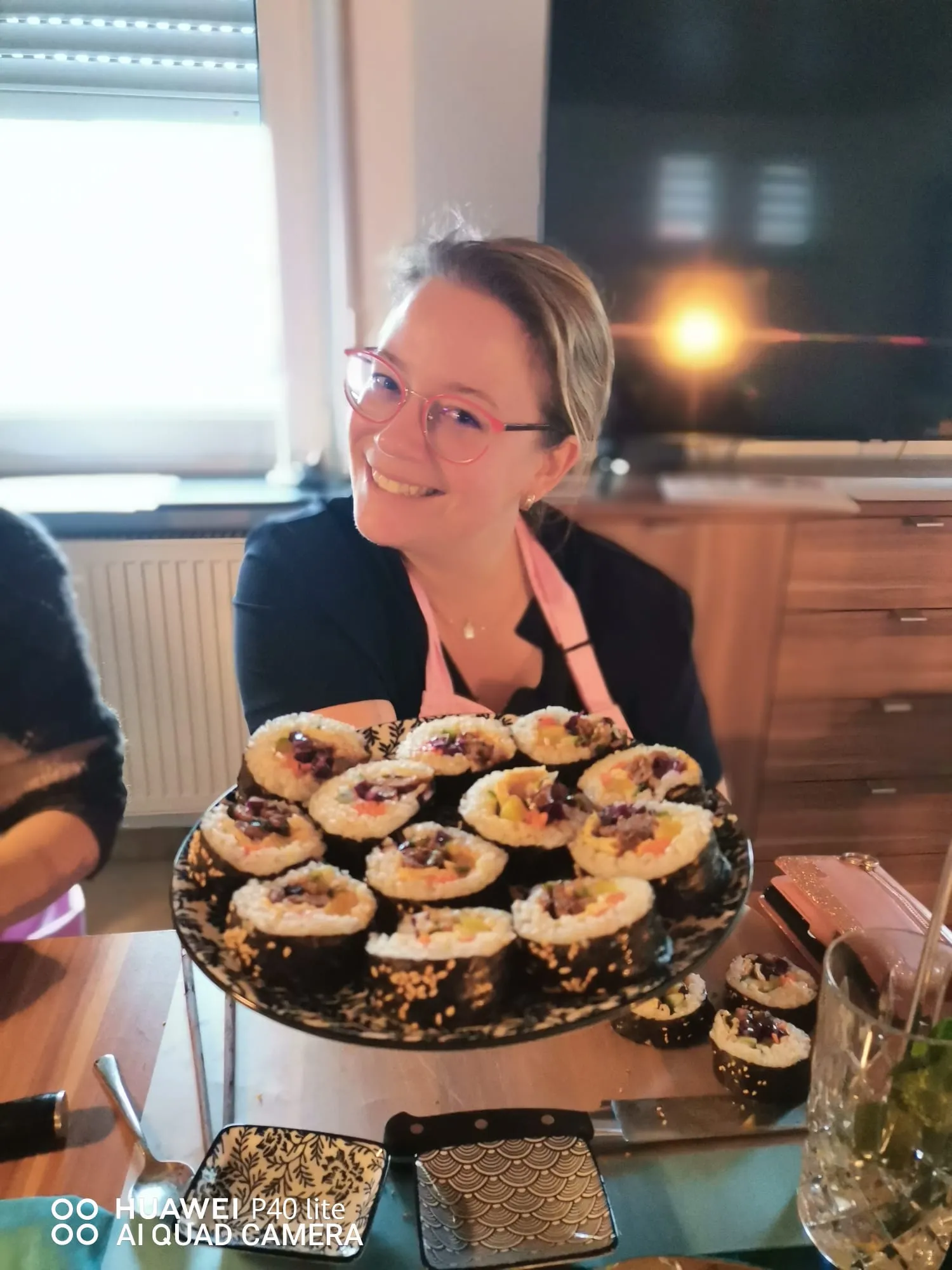 Smiling person holding a plate of sushi rolls.
