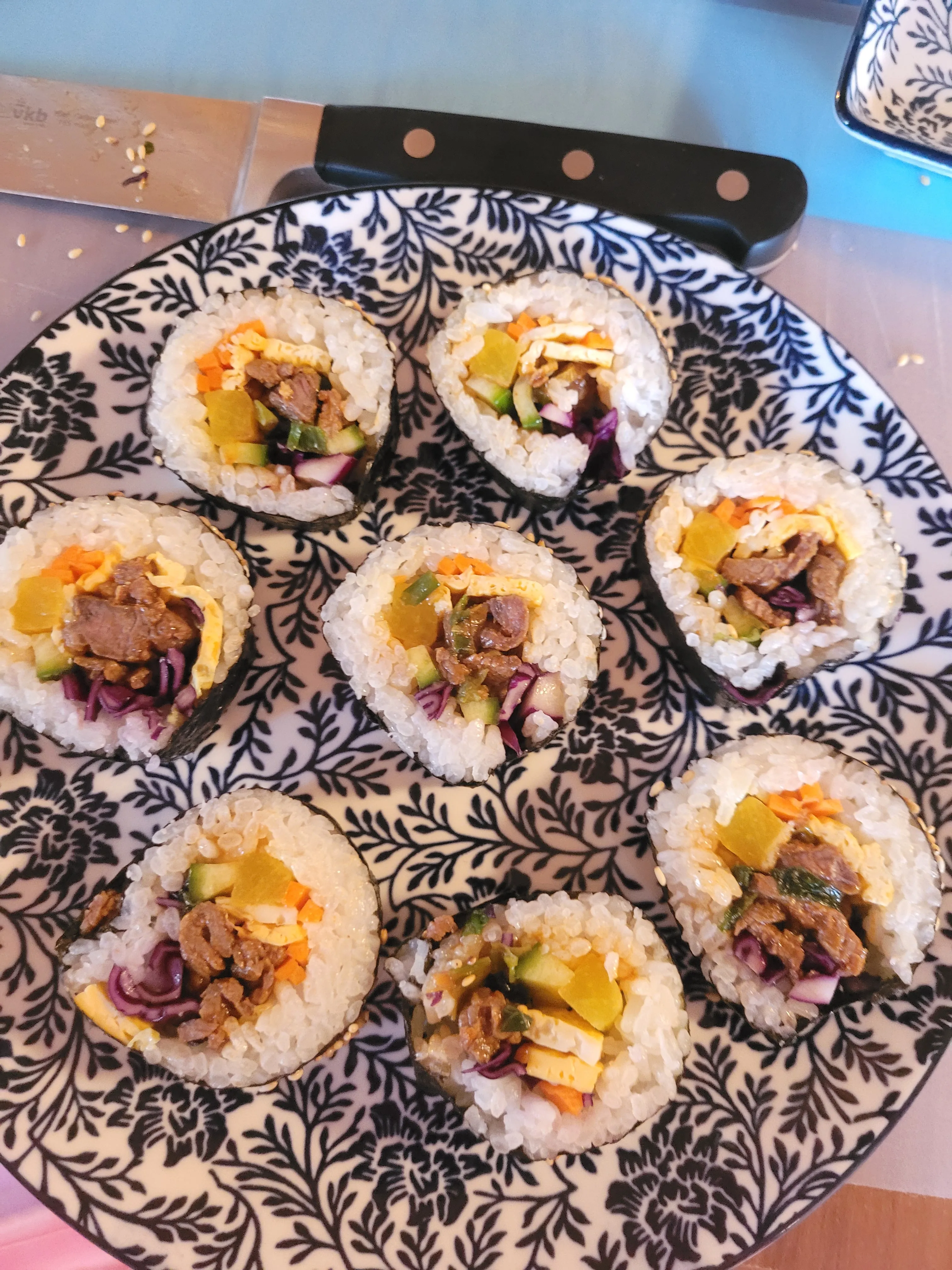 Sushi rolls on decorative plate, knife nearby.