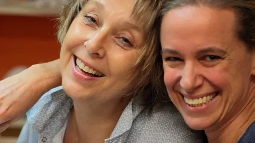 Two women smiling closely together indoors.