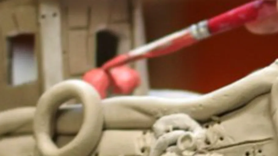 Paintbrush applying red paint on clay sculpture.