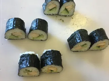 Sushi-Rollen liegen auf einem weißen Schneidebrett.
