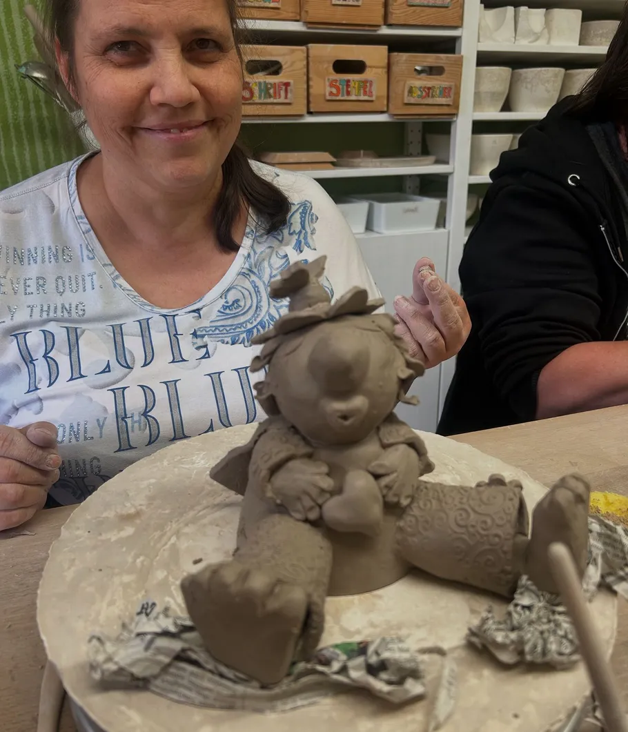 Woman smiling with clay figurine in workshop.