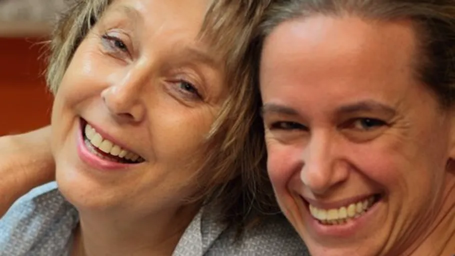 Two smiling women close together indoors.