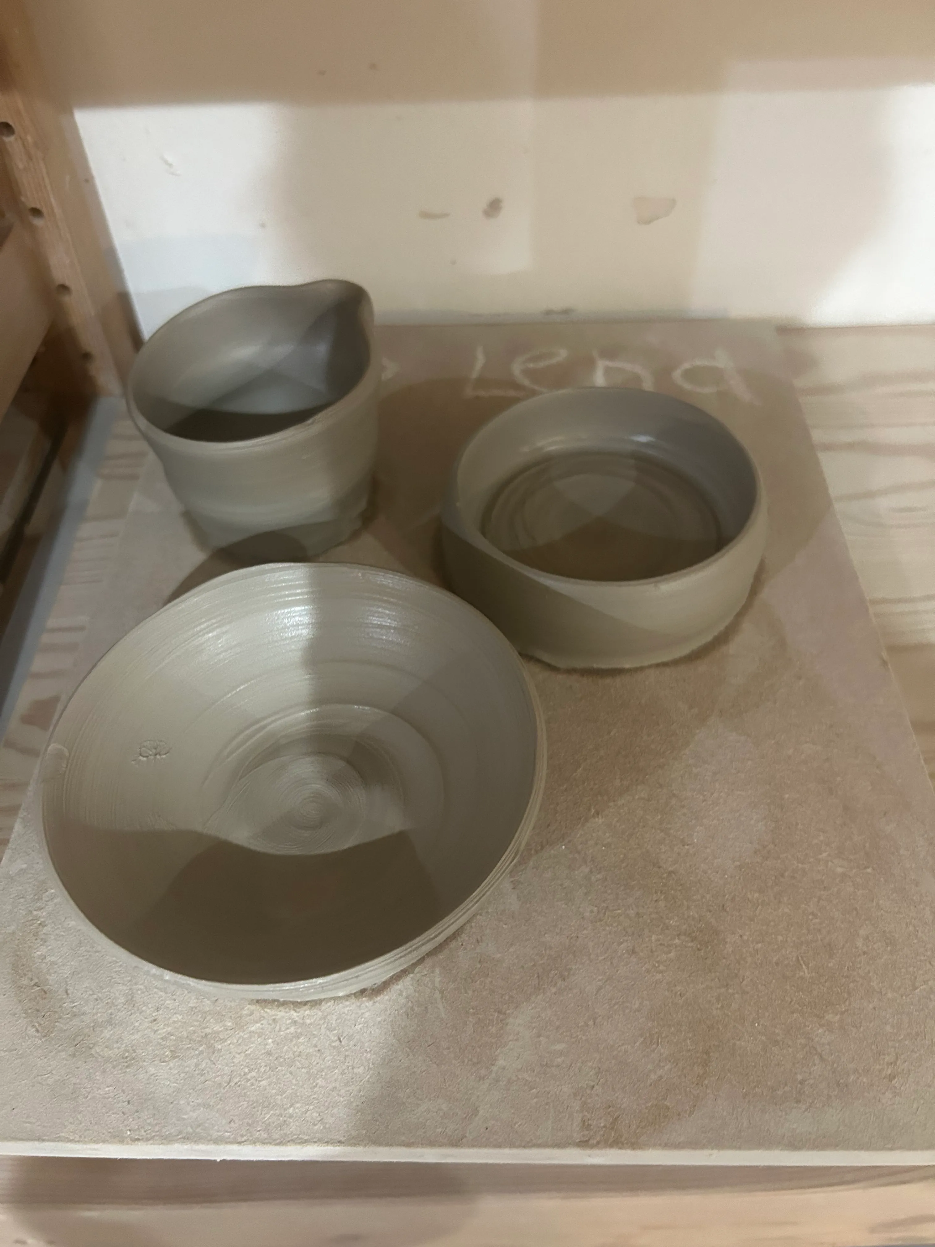 Three clay pots on a wooden shelf.