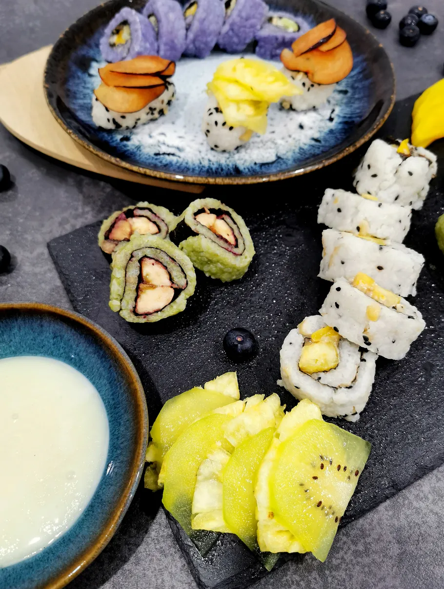 Verschiedene Sushirollen auf Tellern mit Obstscheiben.